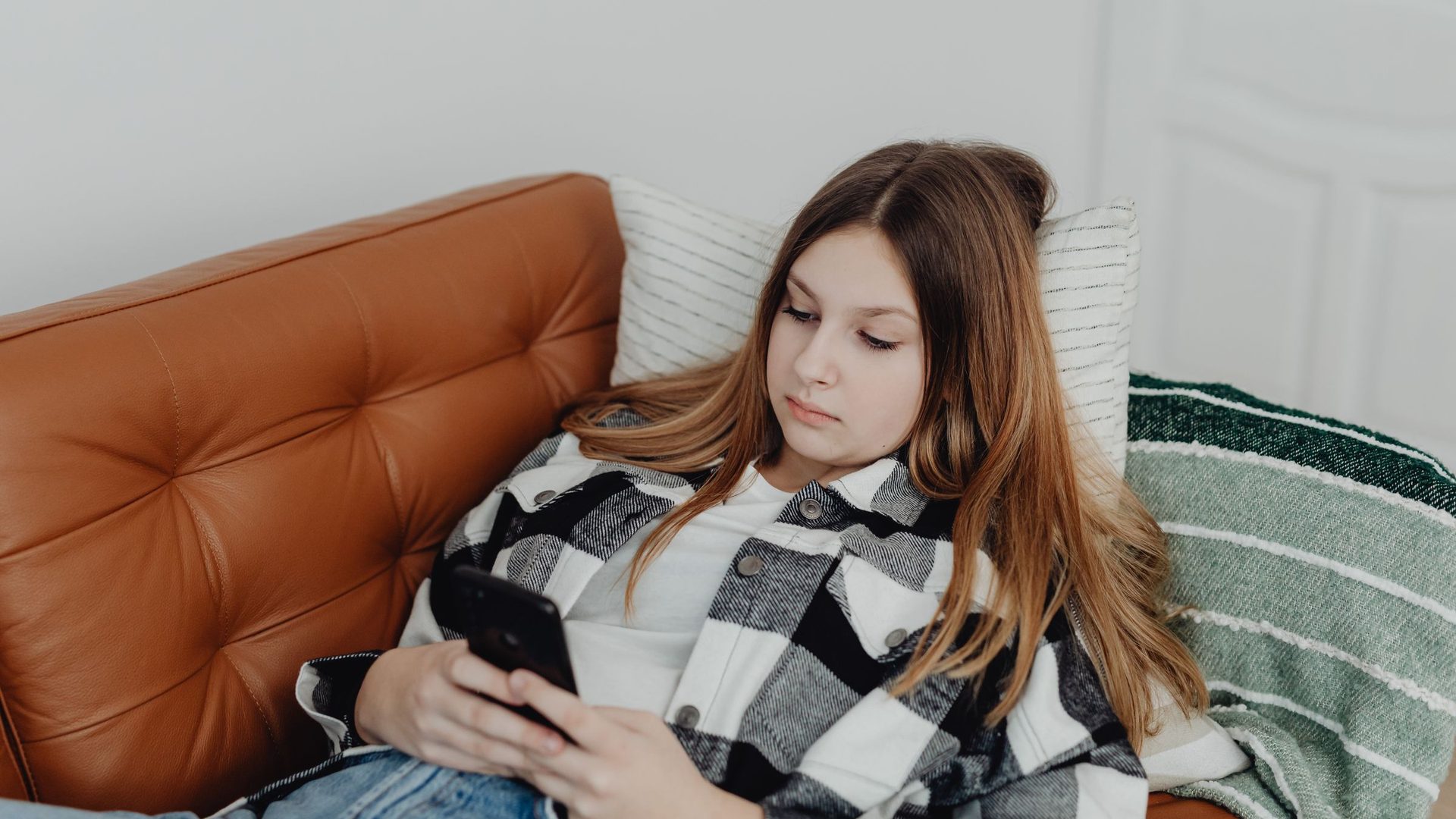Teenage girl lying on a leather couch looking at her phone