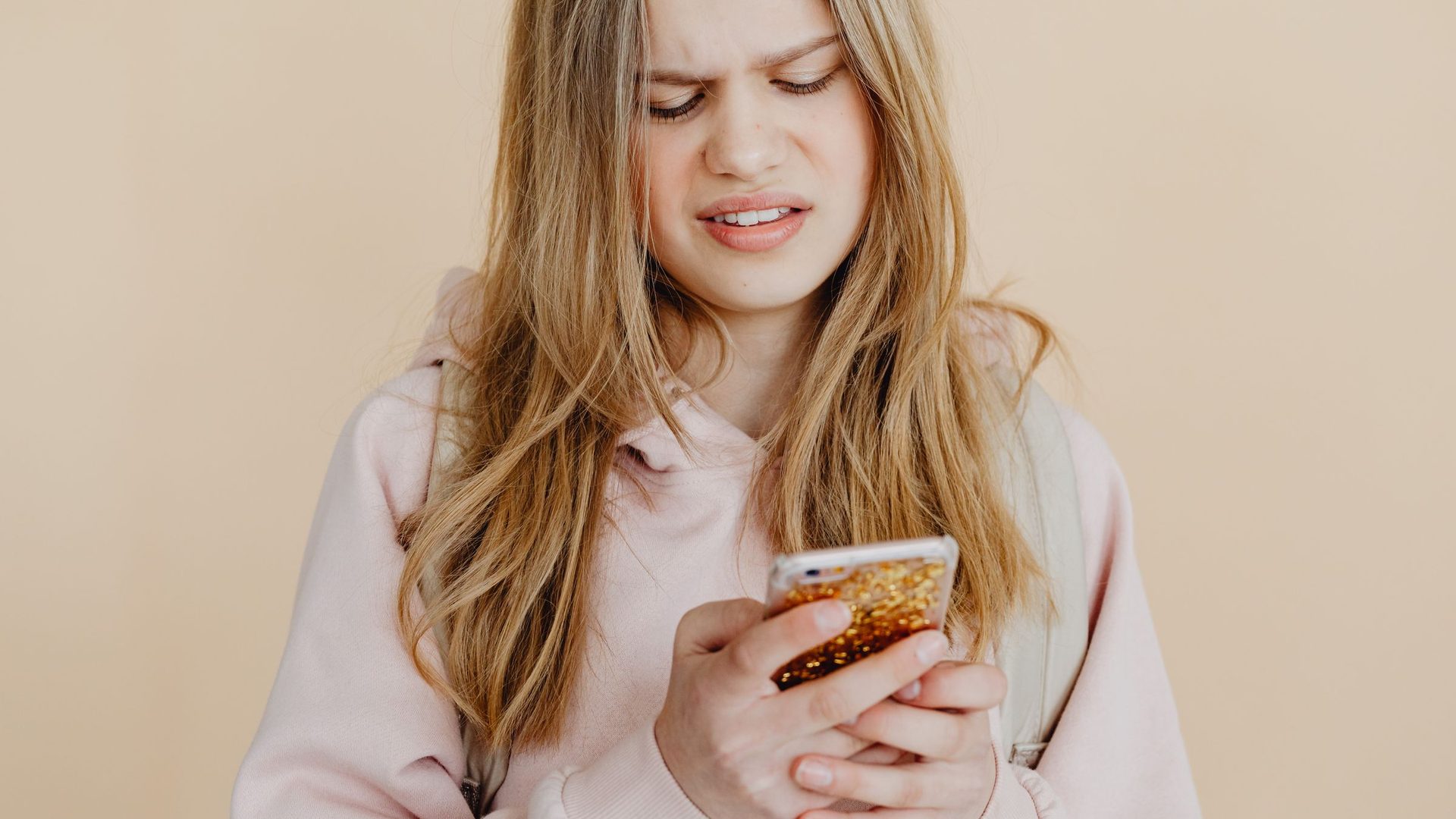 Teenage girl in a pink hoodie frowning at her phone as if reading her results