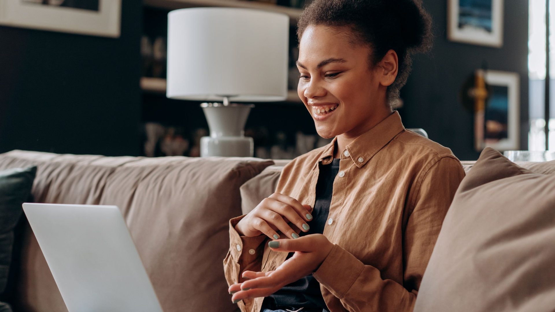 Smiling young woman sitting on a couch and looking at an open laptop
